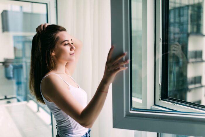 Photo of woman in front of window illustrates blog "How Energy-Efficient Windows Help You Reduce AC Costs"