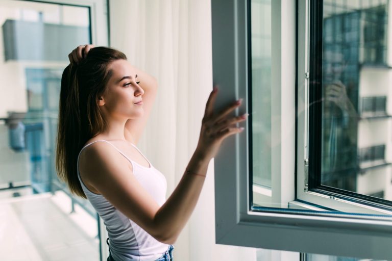 Photo of woman in front of window illustrates blog "How Energy-Efficient Windows Help You Reduce AC Costs"