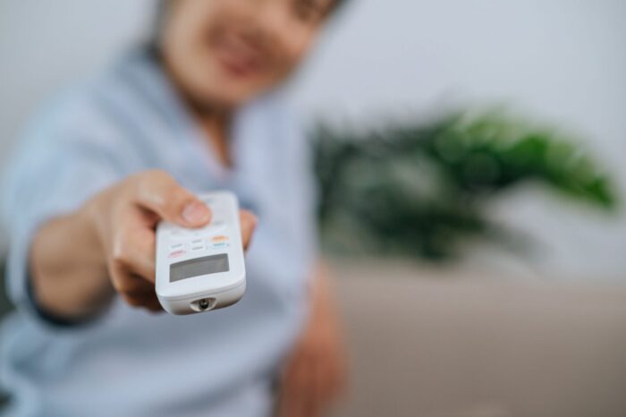 Photo of woman with AC remote illustrates blog: "Why Is My AC Blowing Hot Air?"