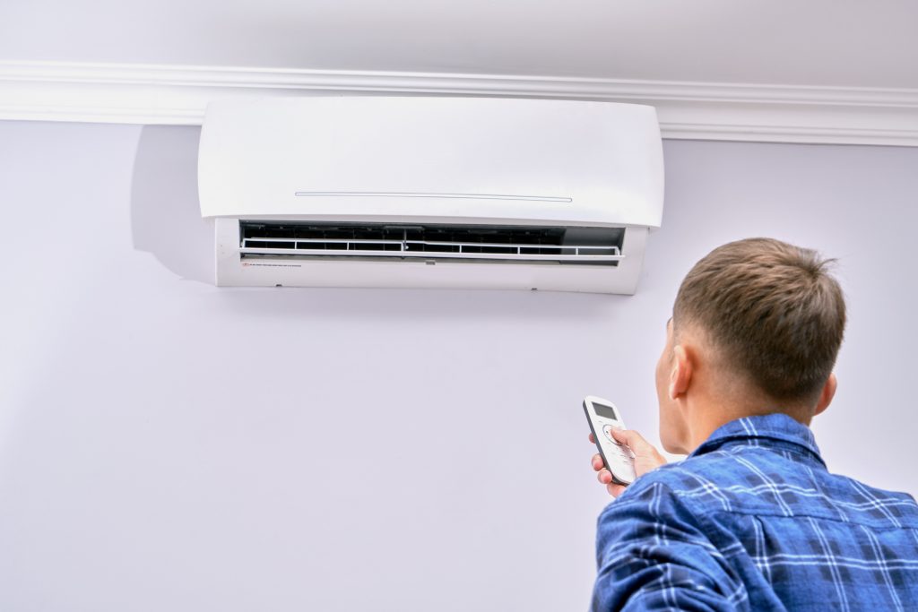 Photo of man with remote control in front of air conditioning illustrates blog: "When was air conditioning invented?"