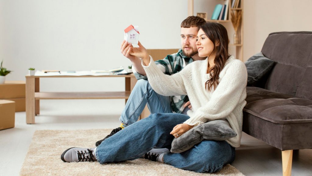 Couple in living room holding a small toy house.