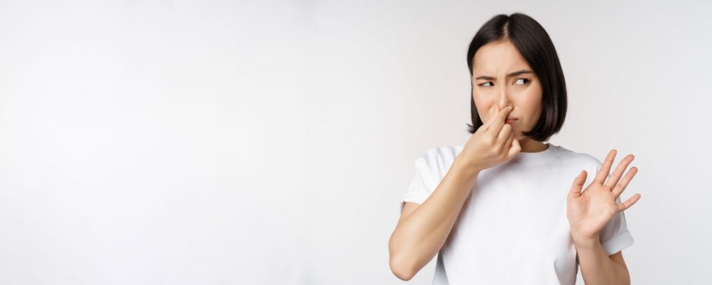 Woman pinching her nose illustrates blog "Should I Turn My AC Off if It Smells?"