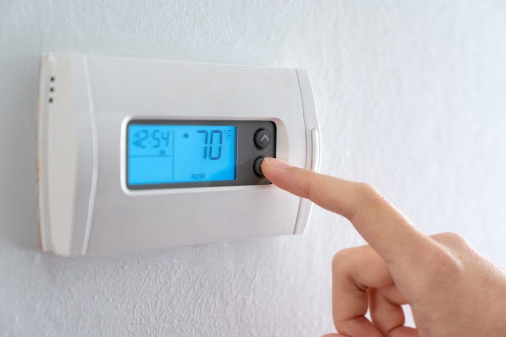 Photo of hand pressing a button on thermostat illustrates blog: "Can I Replace My Thermostat Myself?"