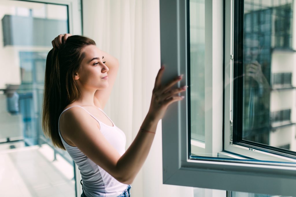 Photo of woman in front of window illustrates blog "How Energy-Efficient Windows Help You Reduce AC Costs"